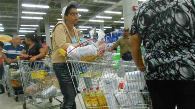 Carrinho com farinha e óleo. Clientes buscam produtos básicos, difíceis de encontrar em supermercado de Caracas