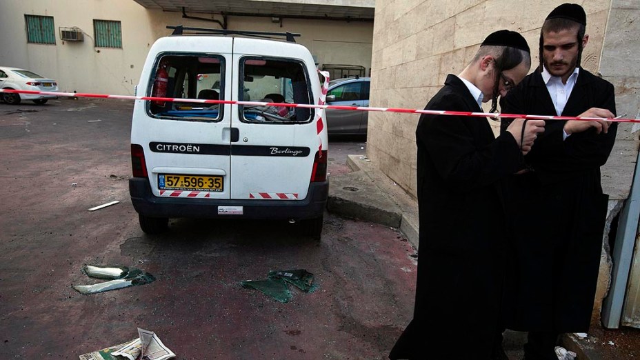 Israelenses ao lado de veículo danificado por foguete lançado por militantes palestinos