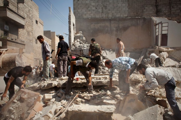 Civis e integrantes do Exército Sírio Livre procuram corpos nos escombros de uma casa destruída por duas bombas da Força Aérea Síria, que tinham como alvo um centro de comando rebelde