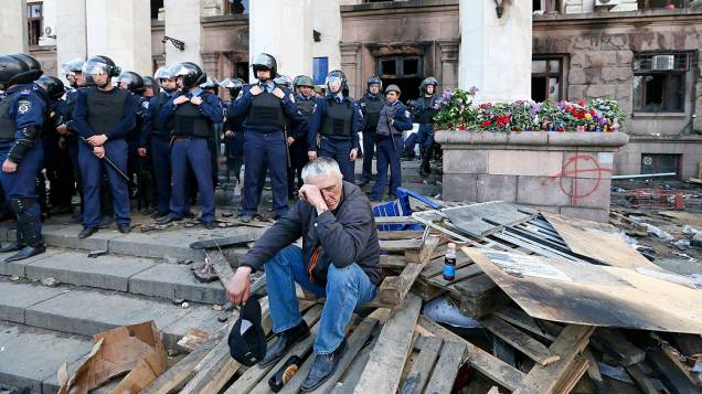 Homem é observado por membros das forças de segurança durante um comício fora do edifício sindical ucraniano que pegou fogo ontem (2) em Odessa, na Ucrânia