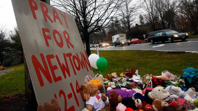 Carro fúnebre carregando o caixão do garoto Jack Pinto de seis anos, passa por um memorial improvisado no caminho para o cemitério de Newtown