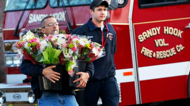 Habitante da cidade de Newtown leva flores para a frente da escola primária Sandy Hook, onde pelo menos 27 pessoas foram mortas nesta sexta