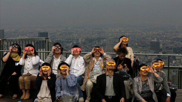 <p>Pessoas assistem ao eclipse anelar no terraço de um prédio em Tóquio, Japão</p>