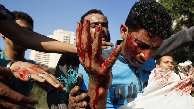 Manifestantes ajudam homem ferido durante conflitos nesta sexta-feira (14), perto da praça Tahir, no Cairo, capital do Egito. Eles protestavam contra filme considerado ofensivo ao Islã