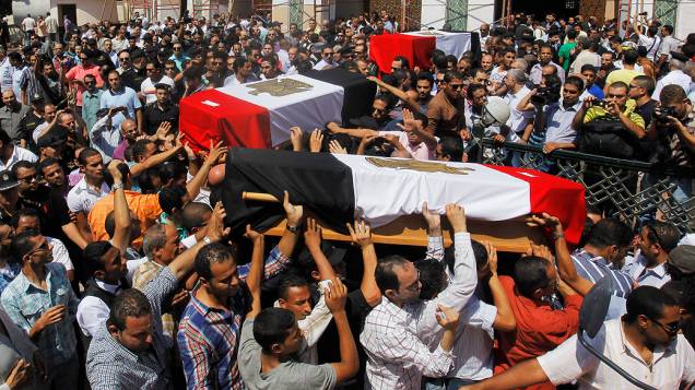Parentes e amigos de policiais que foram mortos durante os confrontos de quarta-feira (14) carregam caixões cobertos com bandeiras do Egito durante um funeral militar no Cairo - (15/08/2013)