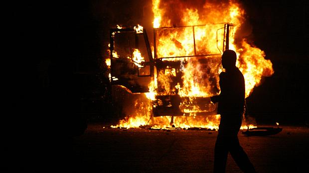Egípcio caminha diante de carro de polícia queimado durante protestos na noite de sexta-feira
