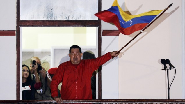 Hugo Chávez segura a bandeira venezuelana ao falar para a milhares de pessoas que se reuniram em Caracas após a confirmação da reeleição do presidente
