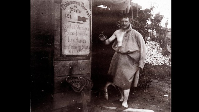 Soldado francês é fotografado depois do banho em retaguarda de front em local não identificado na França. A placa diz: ‘Complexo termal de Poilu. Chuveiros, massagens, pedicure, manicure”