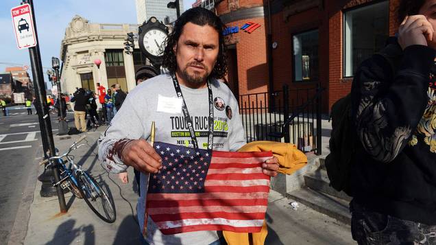 Homem mostra uma bandeira dos Estados Unidos manchada de sangue, após duas explosões na maratona de Boston