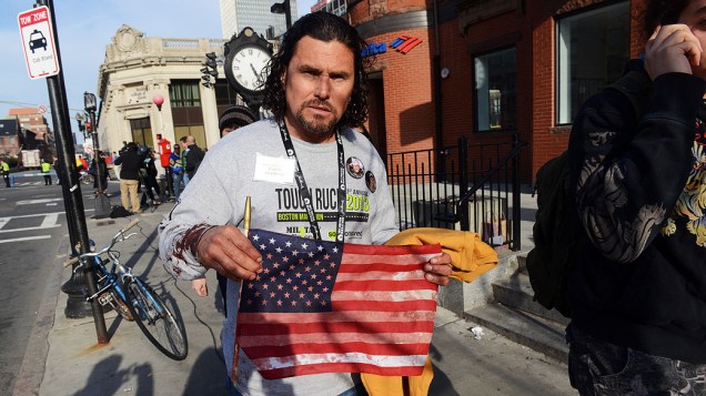 Homem mostra uma bandeira dos Estados Unidos manchada de sangue, após duas explosões na maratona de Boston