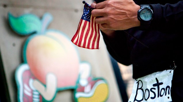 Homem segura a bandeira dos Estados Unidos no local de explosão perto da linha de chegada da Maratona de Boston