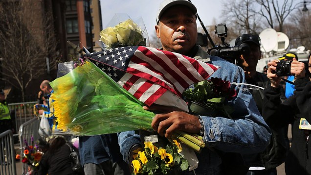 Homem leva flores e bandeira para o memorial das vítimas da explosão na maratona de Boston