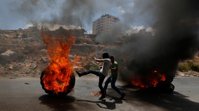 Manifestante palestino chuta um pneu em chamas durante confrontos com tropas israelenses em um protesto contra a ofensiva do país a Gaza, próximo a Ramallah, na Cisjordânia, em 18/07/2014
