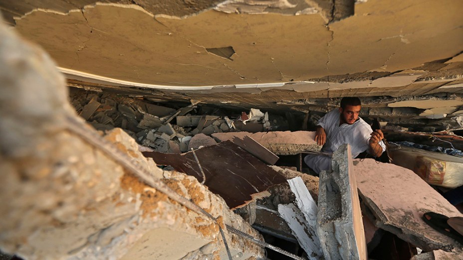 Homem palestino procura pertences sob os escombros de uma casa destruída em um ataque aéreo na cidade de Gaza, em 09/07/2014