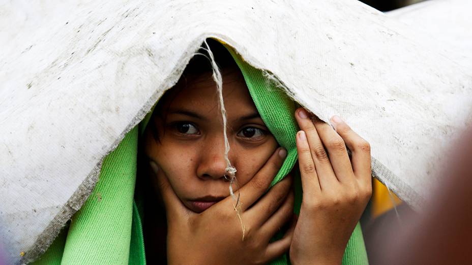 Menino tenta se proteger da chuva antes de embarcar em voo num avião militar usado para retirar pessoas atingidas em Tacloban