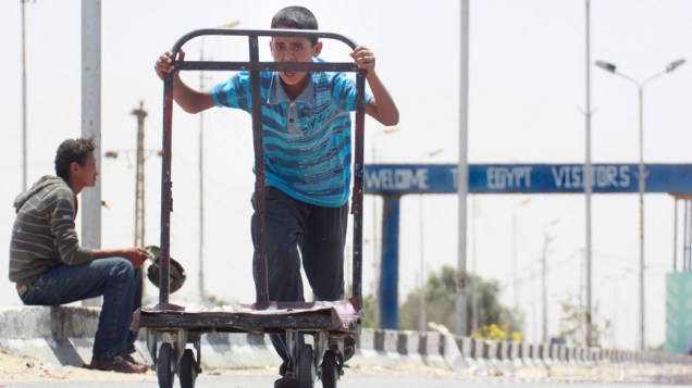 Garoto egípcio trabalha com transporte de bagagens para atender clientes na fronteira com Rafah, na Faixa de Gaza