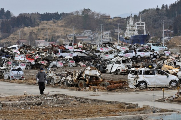 <p>Um homem caminha ao lado de destroços de veículos na região de Miyagi, uma das mais atingidas pelo tsunami que devastou o japão em 11 de março de 2011</p>