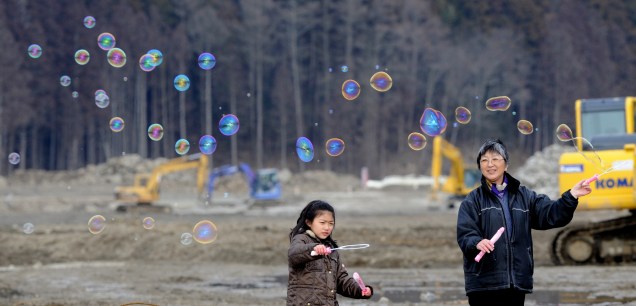 <p>Hiroko Oyama, 58 anos (à direita) e sua neta brincam com bolhas de sabão ao rezar pelas vítimas do desastre que devastou o japão há um ano</p>