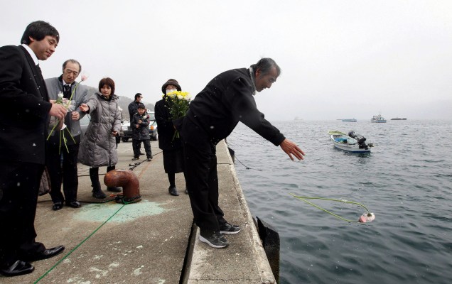 <p>Teruo Shirogane, cuja mãe, esposa e filha foram mortas pelo tsunami, joga uma flor em oferta às vítimas da tragédia na cidade de Otsuchi, na região de Iwate </p>