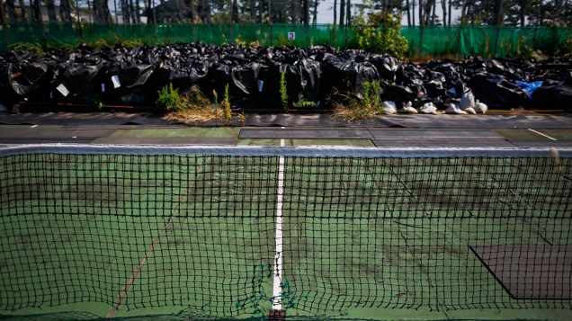 Sacos plásticos com lixo da operação de descontaminação são despejados em quadra de tênis, na cidade Naraha