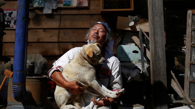 Keigo Sakamoto, 58 anos, com Atom, um de seus 21 cães e mais de 500 animais que ele mantém na zona de exclusão perto de Naraha, em Fukushima