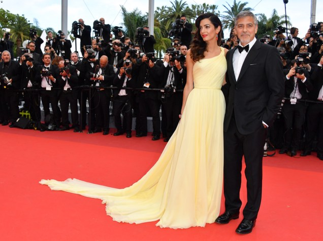 Amal Clooney, sempre elegantérrima, vestiu um Versace amarelo de um ombro só e caimento solto para acompanhar o marido, George Clooney, na première de Jogo do Dinheiro