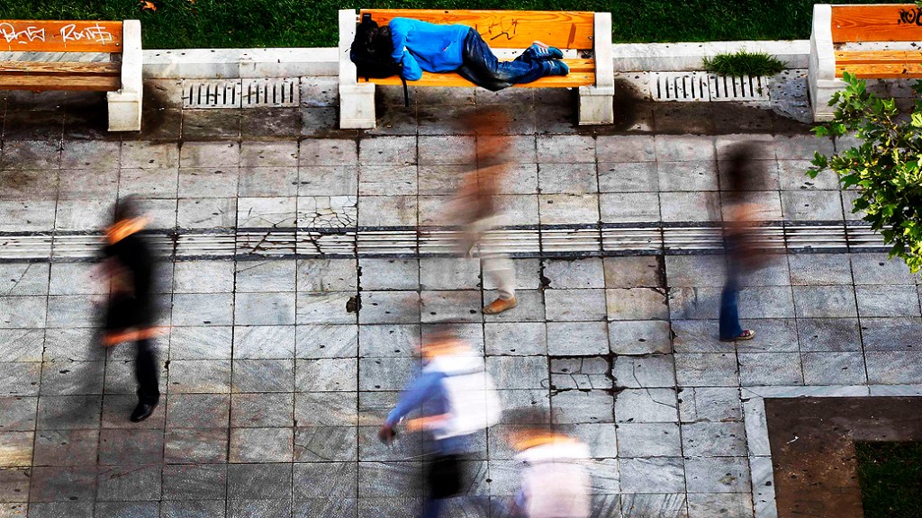 Pessoas caminham perto de sem-teto que dorme na Praça Syntagma, na área central de Atenas, capital da Grécia