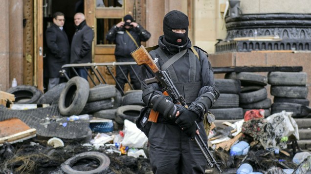 Homem armado representando as forças especiais da Ucrânia monta guarda em frente a um prédio público ocupado anteriormente por manifestantes pró-Rússia