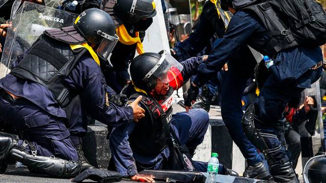 Policiais tailandeses socorrem colega durante confronto com manifestantes em Bangcoc, nesta terça-feira (18)