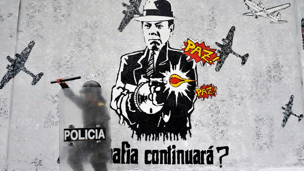 Em Bogotá, um policial fica de guarda ao lado de um grafite contra o presidente colombiano Juan Manuel Santos. O primeiro de maio foi marcado por protestos na capital