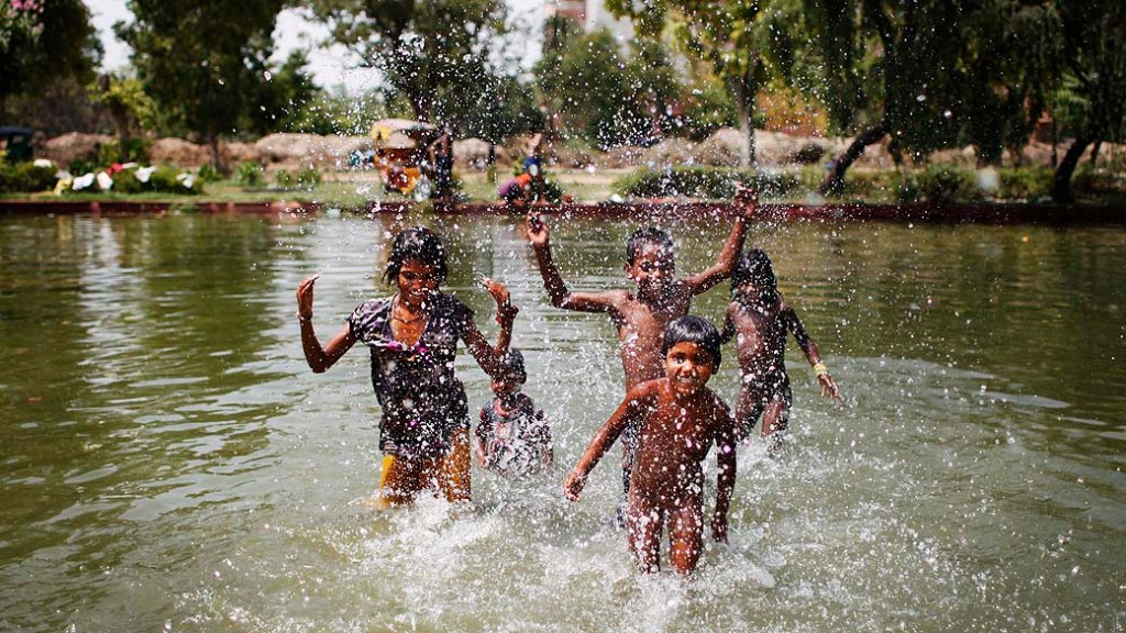 Crianças brincam em lagoa em dia quente de verão em Nova Délhi, na Índia