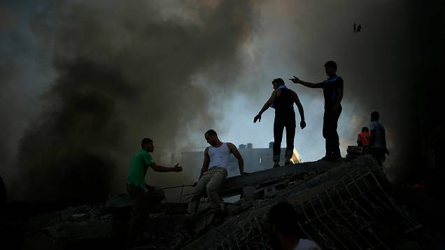 Palestinos tentam extinguir um incêndio após ataque aéreo israelense a um edifício na cidade de Gaza