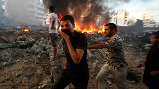 Palestinos passam por edifício incendiado após ataque aéreo israelense na cidade de Gaza