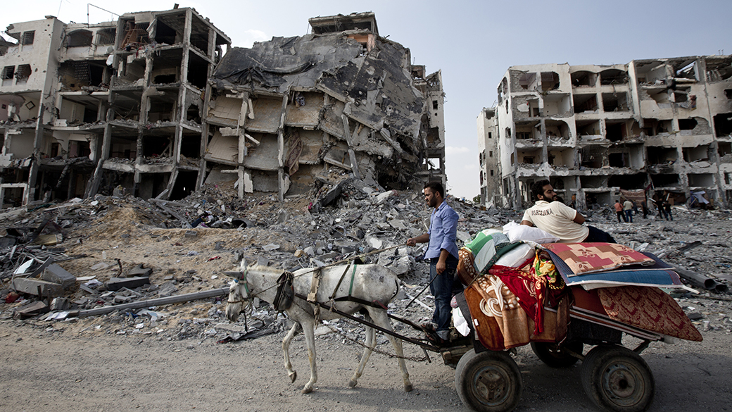 Homens palestinos andam de carroça em meio aos edifícios destruídos no norte da Faixa de Gaza. Israel e o Hamas declararam, nesta terça-feira (05) um cessar-fogo de 72 horas na região