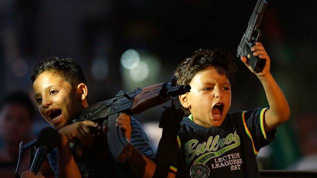 Crianças palestinas seguram armas em comemoração ao acordo de cessar-fogo sem tempo limitado fechado entre Hamas e Israel