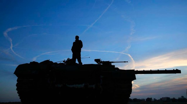 Soldado israelense observa fumaça deixa por caças da Força Aérea durante testes ao norte da faixa de Gaza