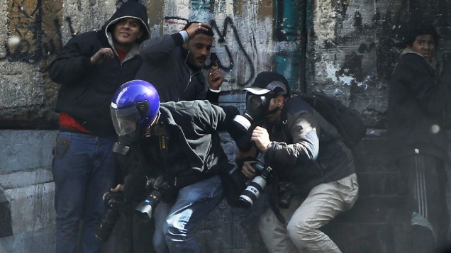 Fotógrafos se protegem enquanto manifestantes atiram pedras em direção a polícia da Praça Tahrir, no Cairo