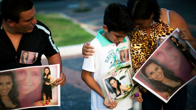 Com um cartaz mostrando foto de vítima do incêndio, menino chora com seus pais em Santa Maria (RS)