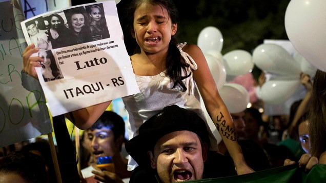Menina chora sobre os ombros do pai segurando um cartaz mostrando fotos de vítimas do incêndio de Santa Maria (RS)