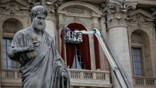 Trabalhadores colocam uma cortina vermelha na bancada central da Basílica de São Pedro, no Vaticano, em preparação à eleição do novo papa ao fim do conclave, que se inicia na terça-feira (12)