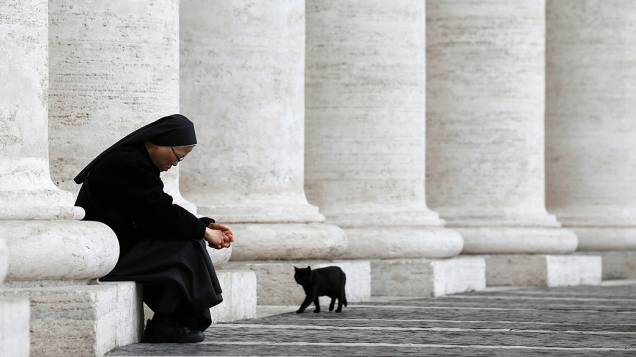 Gato preto caminha ao lado de freira na Praça São Pedro, no Vaticano; O conclave que elegerá o novo papa começará amanhã (12)