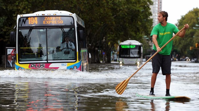 Homem usa prancha para tentar se locomover em avenida alagada. Ao menos cinco pessoas morreram como consequência da forte chuva que atingiu Buenos Aires no início da madrugada desta terça-feira (2)