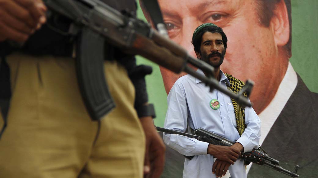 Policial e segurança particular perto do retrato de Nawaz Sharif, líder do partido Liga Muçulmana do Paquistão-Nawaz (PML-N), durante um comício de campanha eleitoral em Peshawar. As eleições gerais do Paquistão serão realizadas no dia 11 de maio