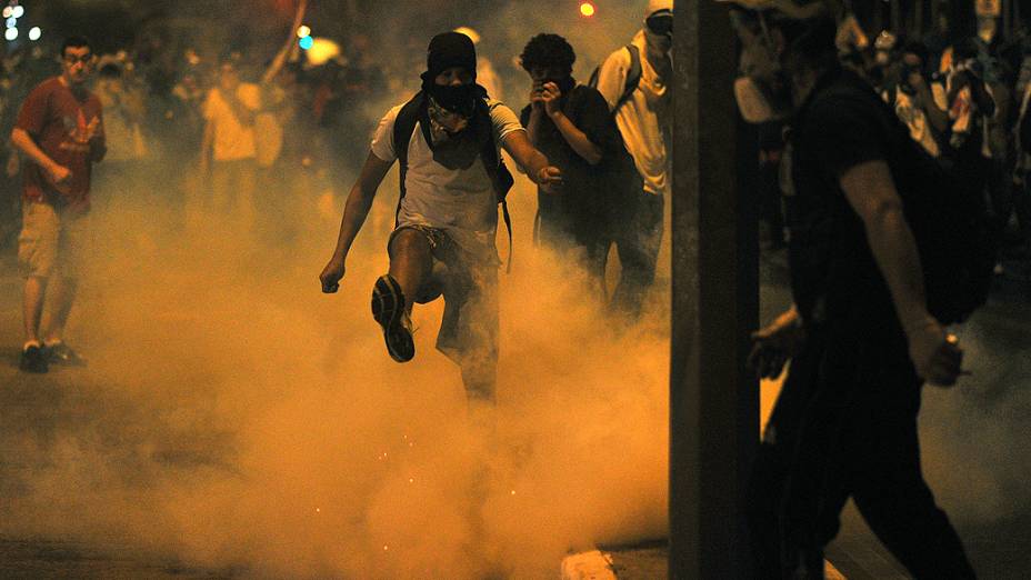 Manifestante chuta uma bomba de gás lacrimogêneo durante confrontos com a polícia do lado de fora do estádio Mineirão, em Belo Horizonte, na quarta-feira (26)