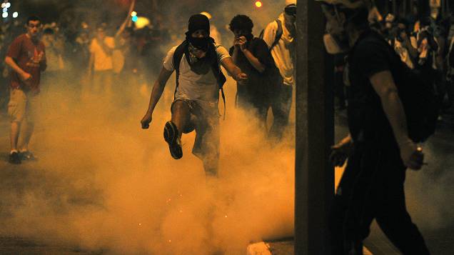 Manifestante chuta uma bomba de gás lacrimogêneo durante confrontos com a polícia do lado de fora do estádio Mineirão, em Belo Horizonte, na quarta-feira (26)