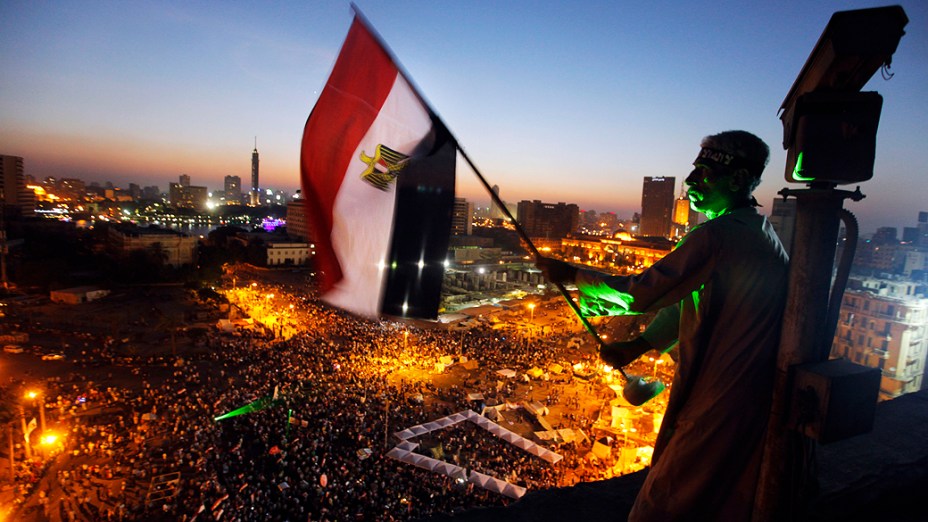 Manifestante segura a bandeira egípcia no alto de prédio perto da Praça Tahrir, local de reunião dos opositores do presidente Mohammed Mursi, na sexta-feira (28)