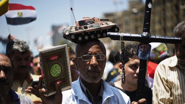 Homem com um tanque de brinquedo na cabeça, segura uma cruz e uma cópia do Corão, caminha até a praça Tahrir, no Cairo nesta quinta-feira (04), depois de uma noite de celebrações após a derrubada do deposto presidente egípcio Mohammed Mursi