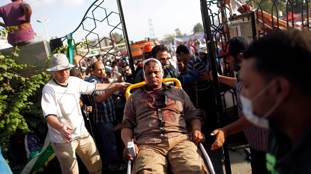 Homem ferido é transferido de cadeiras de rodas a hospital improvisado, após tiroteio próximo da Guarda Republicana do Egito, no Cairo; ao menos 34 morreram