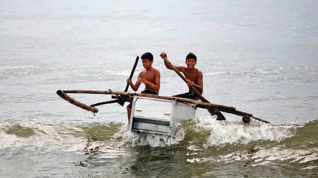 Garotos conduzem barco feito de uma geladeira quebrada e bambu na praia em Tanauan, nas Filipinas, nesta quarta-feira (20)