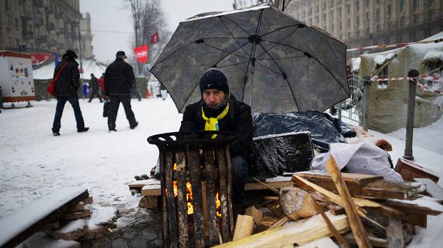 Manifestante se aquece na manhã desta segunda-feira (9) enquanto guarda barricada de protesto, na praça da Independência, em Kiev (Ucrânia)
